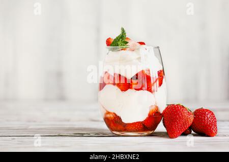 Sana prima colazione di fragole parfait a base di frutta fresca, e yogurt su un rustico tavolo bianco. Messa a fuoco selettiva con sfondo sfocato. Foto Stock