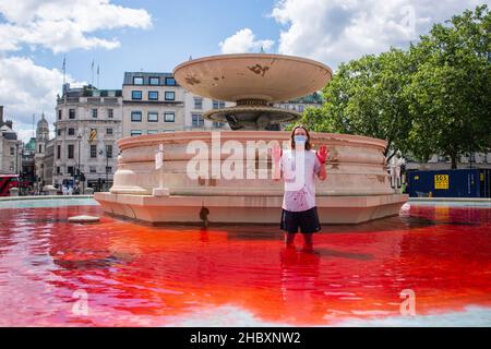 Attivista della ribellione degli animali in piedi in acqua rossa nella fontana di Trafalgar Square che tiene le mani in Air London 2020 Foto Stock