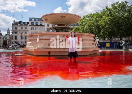 Attivista della ribellione degli animali in piedi in acqua rossa nella fontana di Trafalgar Square che tiene le mani in aria Londra 2020 Foto Stock