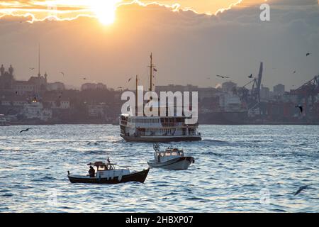 Pescatori in barche da pesca e traghetti di linea della città nel Bosforo all'alba in inverno mattina a Istanbul, Turchia il 21 dicembre 2021. Foto Stock