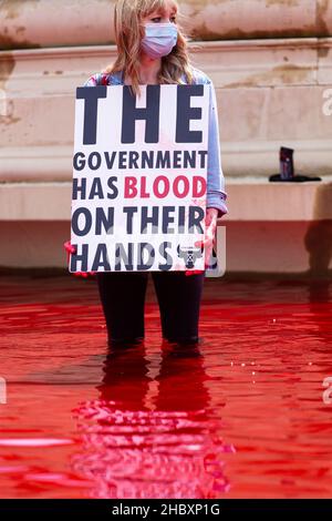 Attivista della ribellione degli animali in piedi in acqua rossa nella fontana di Trafalgar Square che tiene sangue sulle mani placard London 2020 Foto Stock