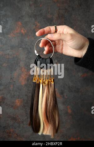 La mano femminile tiene i campioni di capelli su sfondo scuro Foto Stock