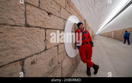 22 dicembre 2021, Sassonia, Chemnitz: L'artista Anke Neumann si trova nel nuovo tunnel pedonale della stazione centrale di Chemnitz. Lo stretto tunnel tra il centro della città e il quartiere Sonnenberg è stato migliorato, tra le altre cose, da un nuovo concetto di illuminazione. Inoltre, lettere bianche alte 1,40 metri sulle pareti formano una citazione dalla canzone 'Wie ich' della band Kraftklub: 'ICH wär'gern weniger wie ich, ein bisschen mehr so wie du'. Nella volgare, il sottopasso, precedentemente piuttosto scuro, lungo 220 metri, è comunemente conosciuto come il 'tubo germinale'. In due fasi di costruzione, il entra Foto Stock