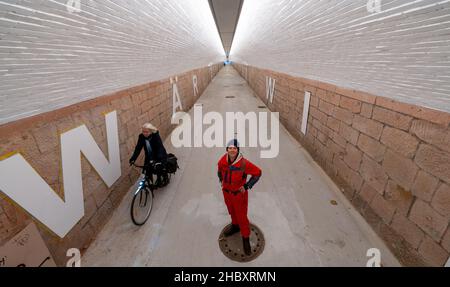 22 dicembre 2021, Sassonia, Chemnitz: L'artista Anke Neumann si trova nel nuovo tunnel pedonale della stazione centrale di Chemnitz. Lo stretto tunnel tra il centro della città e il quartiere Sonnenberg è stato migliorato, tra le altre cose, da un nuovo concetto di illuminazione. Inoltre, lettere bianche alte 1,40 metri sulle pareti formano una citazione dalla canzone 'Wie ich' della band Kraftklub: 'ICH wär'gern weniger wie ich, ein bisschen mehr so wie du'. Nella volgare, il sottopasso, precedentemente piuttosto scuro, lungo 220 metri, è comunemente conosciuto come il 'tubo germinale'. In due fasi di costruzione, il entra Foto Stock