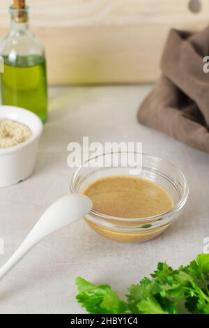 Tahini in un recipiente di vetro con ingredienti ed erbe su sfondo chiaro. Salsa asiatica tradizionale per fare l'hummus. Concetto di cucina Levantine. Vegetar Foto Stock
