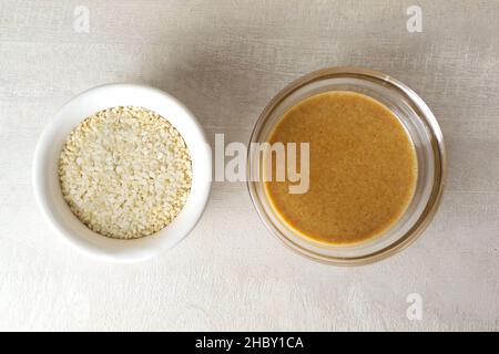 Tahini in una ciotola di vetro con semi di sesamo in una ciotola bianca su sfondo chiaro. Salsa asiatica tradizionale per fare l'hummus. Concetto di cucina Levantine. Foto Stock