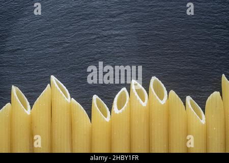 Penne bordo di pasta isolato su una mattonella nera, tessuto di pietra Foto Stock