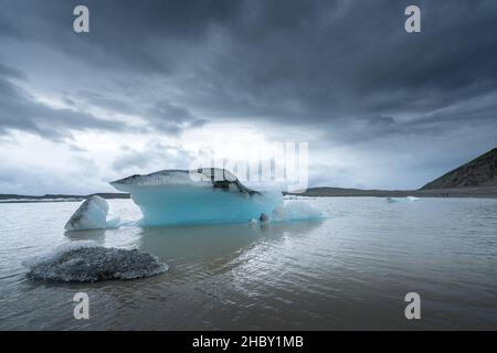 Il ghiaccio galleggia nelle acque fangose del lago glaciale con il ghiacciaio sullo sfondo in una giornata nuvolosa e piovosa. Fjallsarlon, Islanda. La gente piccola che guarda dal Foto Stock