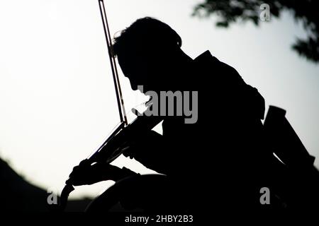 silhouette di un giovane maschio che gioca violino in un parco Foto Stock