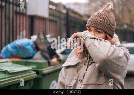 Primo piano di donna senza casa pulizia volto sporco con la mano dopo la ricerca di cibo in lattine spazzatura. Foto Stock