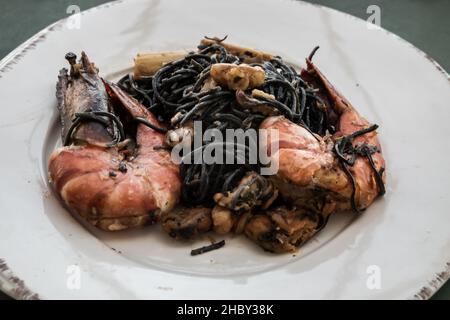 Spaghetti con inchiostro calamaro (spaghetti neri) con gamberi fluviali o gamberetti, cozze e bambù sparare servito su piatto di ceramica bianca. Cibo sano da mangiare, Foto Stock