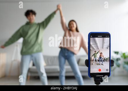 Coppia di influencer asiatici sparare video danza per social network sul cellulare, divertirsi a casa, fuoco selettivo Foto Stock