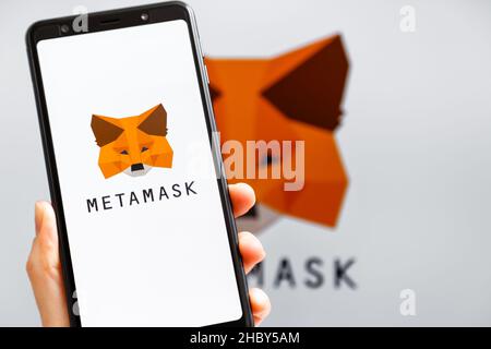 Ucraina, Odessa - Ottobre, 9 2021: Tenere la mano mobile con l'app MetaMask in esecuzione sullo schermo dello smartphone con il logo MetaMask sullo sfondo. MetaMask è così Foto Stock
