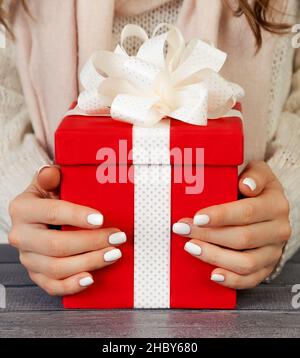 Mani femminili che tengono una scatola regalo rossa con un nastro bianco. Christm Foto Stock