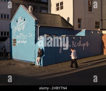 Utenti di telefonia mobile al di fuori di un negozio di Fish and chip al porto, Whitby, North Yorkshire, Regno Unito Foto Stock