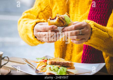 Donna che fa colazione in un caffè all'aperto in via città. Sandwich e caffè sul tavolo. Foto Stock