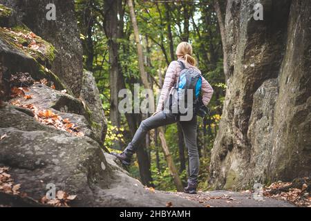 Donna con zaino che viaggia nella foresta. L'escursionista femminile è in piedi tra le rocce in montagna. Foto Stock