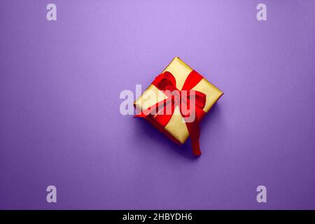 Regalo di festa. Confezione regalo in oro con arco rosso, su sfondo pantone. Buon Natale San Valentino saluti. Cartolina con amore. Foto Stock