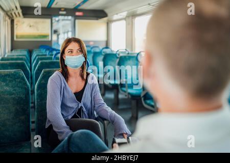 Un paio di viaggiatori che indossano la maschera che chiacchierano in un treno, Portogallo Foto Stock