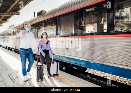 Turisti con valigie e maschere sulla piattaforma accanto al treno, Portogallo Foto Stock