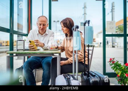 Un paio di viaggiatori che bevono caffè e controllare qualcosa al telefono, il bagaglio con maschere in primo piano, Portogallo Foto Stock