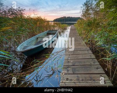 Atmosfera serale al Grosser Lychensee, molo in legno e barca a remi in canne, Lychen, Brandeburgo, Germania Foto Stock