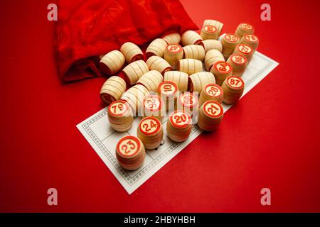 Barili di bingo in legno, su sfondo rosso in una borsa rossa, per giocare a bingo. Un modo per trascorrere il tempo a casa. Un gioco del caso, carta con numeri. Foto Stock