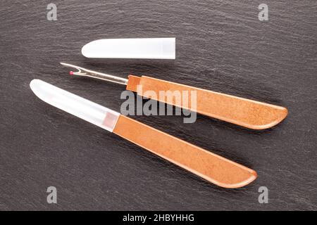 Due coltelli da cucire per tagliare i fili su una pietra ardesia, primo piano, vista dall'alto. Foto Stock