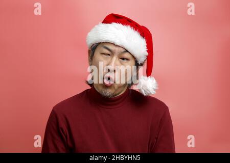 Il ritratto asiatico uomo con cappello babbo natale su sfondo rosa. Foto Stock