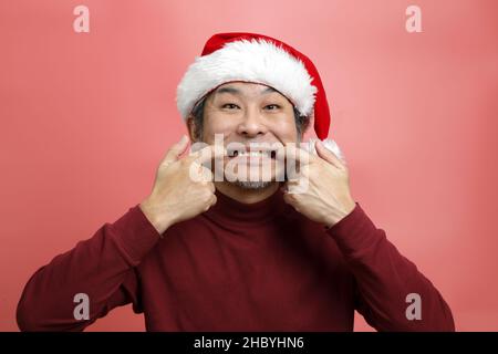 Il ritratto asiatico uomo con cappello babbo natale su sfondo rosa. Foto Stock