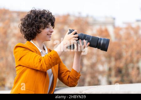 Giovane donna brunetta con capelli ricci che scatta una foto con teleobiettivo Foto Stock