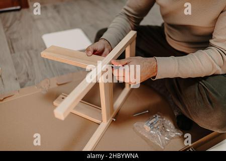 Un uomo esperto assembla mobili di legno con una chiave esagonale a casa Foto Stock