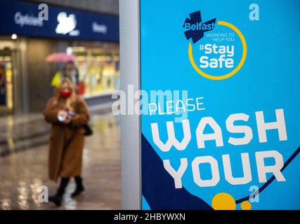 Una donna passa davanti a un messaggio di sicurezza del Covid dal consiglio comunale di Belfast. Foto Stock