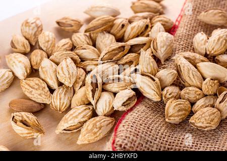 Noci di mandorle marroni arrostite in guscio incrinato su sfondo chiaro tavolo pronto a mangiare. Foto Stock