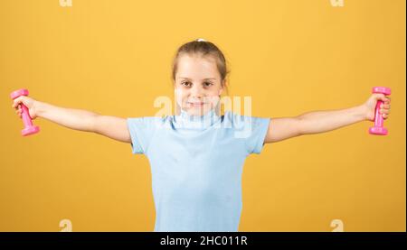 Fitness bambino. Ritratto di bambina sportiva con manubri su sfondo giallo studio isolato. Allenamento in palestra. Sportivo bambino, attività di infanzia Foto Stock