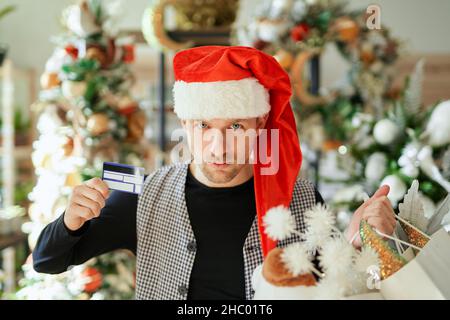 Vendita di Natale e concetto di shopping. Uomo caucasico con borse shopping e carta di credito, indossare cappello Santa sul centro commerciale o sfondo decorazione di Natale. Offerta speciale Natale per i clienti Foto Stock