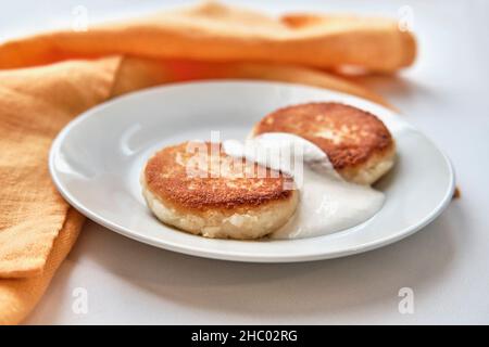 Due cheesecake con panna acida su un piatto bianco. Concetto di colazione. Foto Stock