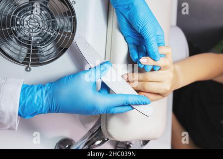 Manicurista limatura giovane donna chiodi in salone indossare guanti protettivi blu fare chiodi pronti per lucidare. Foto Stock