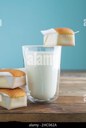 Cupcake fatti in casa con un bicchiere di latte su un tavolo di legno con sfondo blu. Spazio di copia. Foto verticale. Madeleine fatte a mano. Foto Stock
