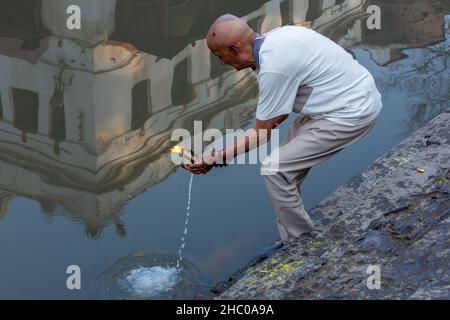 Un uomo indù fa un'offerta religiosa nel fiume Bagmati dal complesso del tempio di Pashupatinath, Kathmandu, Nepal. Foto Stock