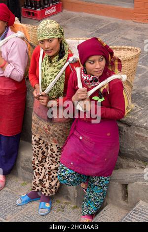 Due giovani donne nepalesi riposano dal trasporto di pesanti cesti di pietre sulle loro spalle su scale a Kathmandu, Nepal Foto Stock