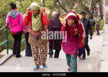 Due giovani donne nepalesi trasportano pesanti cesti di pietre sulle loro spalle su scale usando una tumpline a Kathmandu, Nepal Foto Stock