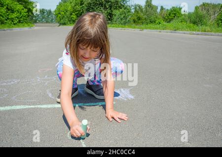 Una bambina disegna con gesso su una strada asfaltata. Concetto - disegni per bambini di un'immagine su asfalto. Foto Stock