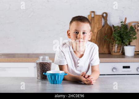 Un ragazzo biondo si trova vicino ad un vaso di cereali al cioccolato e ad una ciotola. Concetto di colazione. Foto Stock