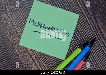 Le microaggressioni scrivono su note appiccicose isolate su tavola di legno. Foto Stock