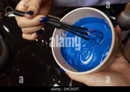 ragazza in guanti di protezione in gomma bianca tenendo una spazzola nelle sue mani e mescolando tintura capelli primo piano-up colorist Foto Stock