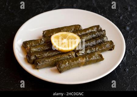 Deliziosa dolma (sarma) ripiena d'uva lascia il riso, salsa di yogurt bianco. Foglie d'uva farcite su sfondo scuro. Dolma sarma libanese sul piatto. Libano Foto Stock