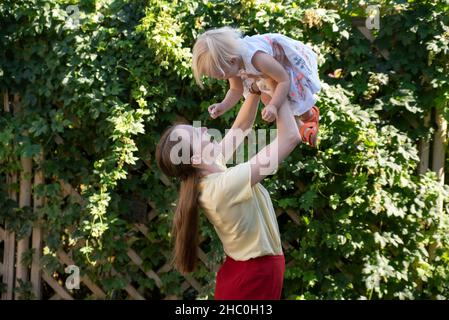 La mamma lancia il bambino nell'aria. La madre cerchia il bambino tra le braccia. Ritratto di felice mummia e capretto Foto Stock