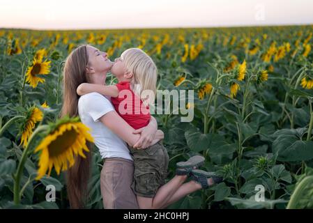 Mamma e figlio si abbracciano nel campo tra i girasoli. Una famiglia felice. Foto Stock
