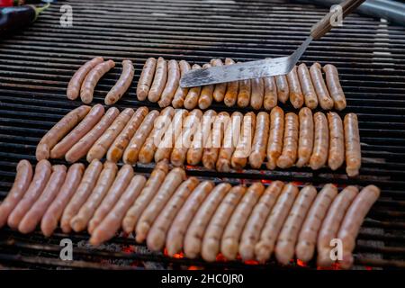 Chef grigliare salsicce di carne fresca su un grande grill rotondo - primo piano Foto Stock